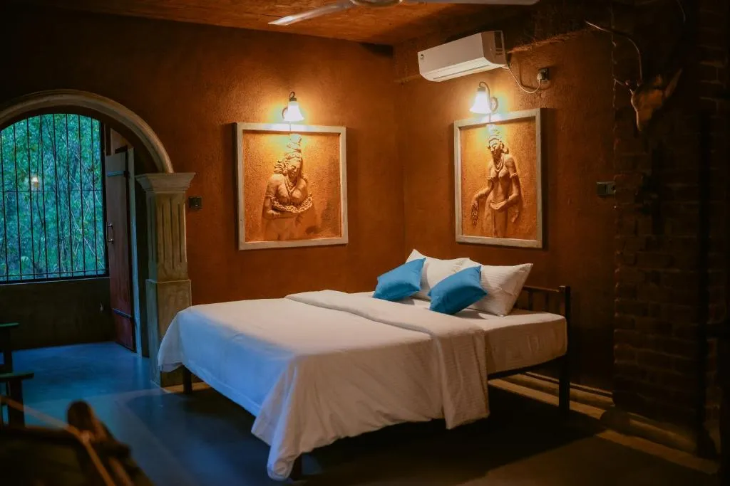A cottage bedroom with air conditioning, a ceiling fan and two framed clay reliefs above the bed