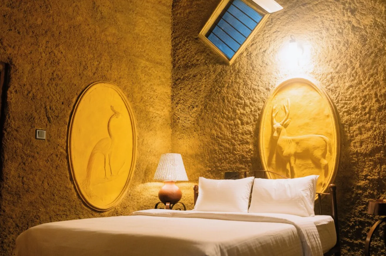 The Double Room Cottage bedroom at Sigiriya Wild Cottages, a queen bed under a carved deer, with a peacock relief beside it