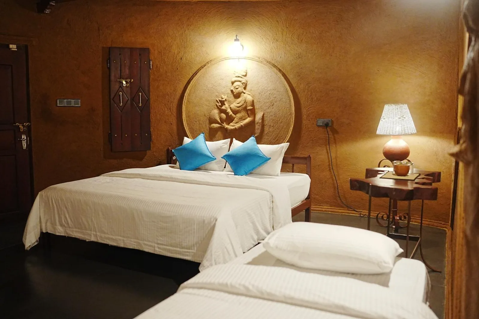 Inside the Triple Room Cottage at Sigiriya Wild Cottages, a king bed under a carved figure and a separate single bed