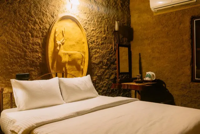 The queen bed in the Double Room Cottage, with a carved deer on the clay wall and a desk beside it