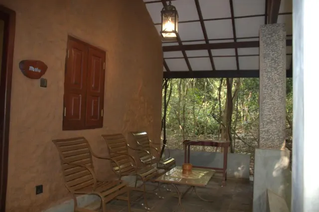 Slatted chairs and a low table under the covered roof beside the Double Room Cottage, with a lantern overhead