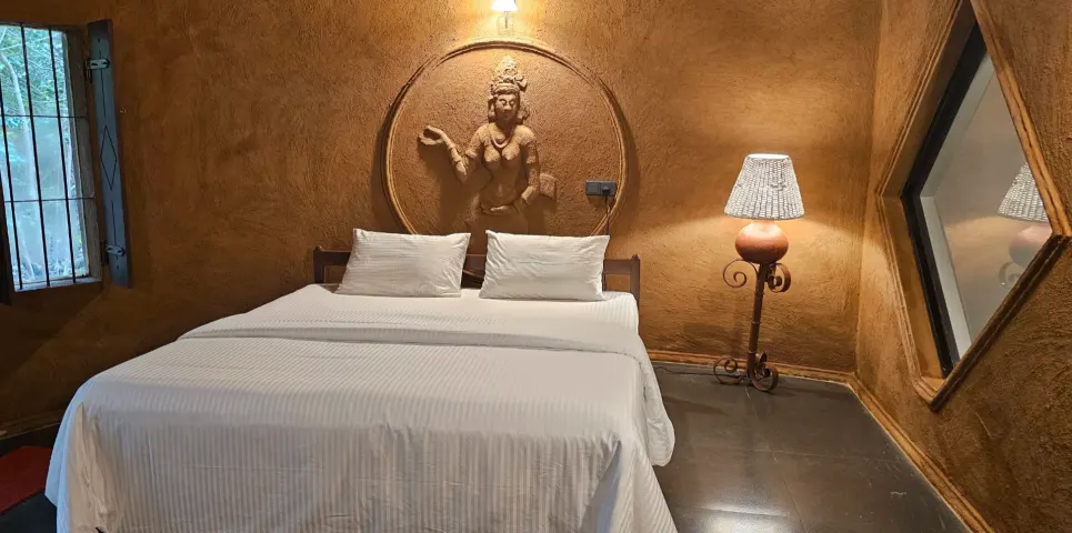 The king bed in the Triple Room Cottage under a carved figure, with a standing lamp beside it