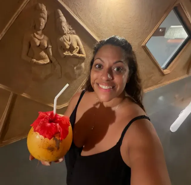 A guest holding a king coconut with a hibiscus flower, in front of a carved relief of two figures