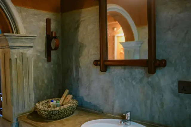 A cottage bathroom with a wooden-framed mirror over the basin and toiletries in a stone bowl