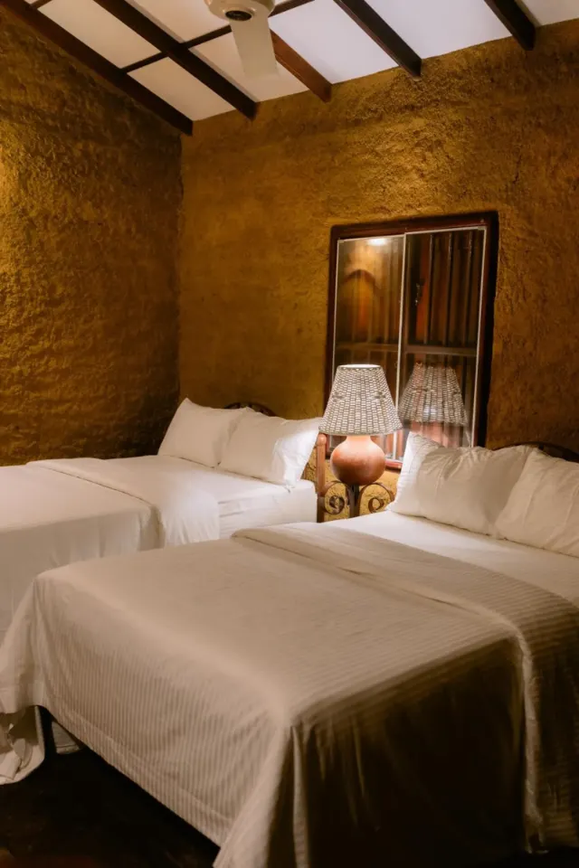 Two double beds under a sloping, beamed ceiling with a fan