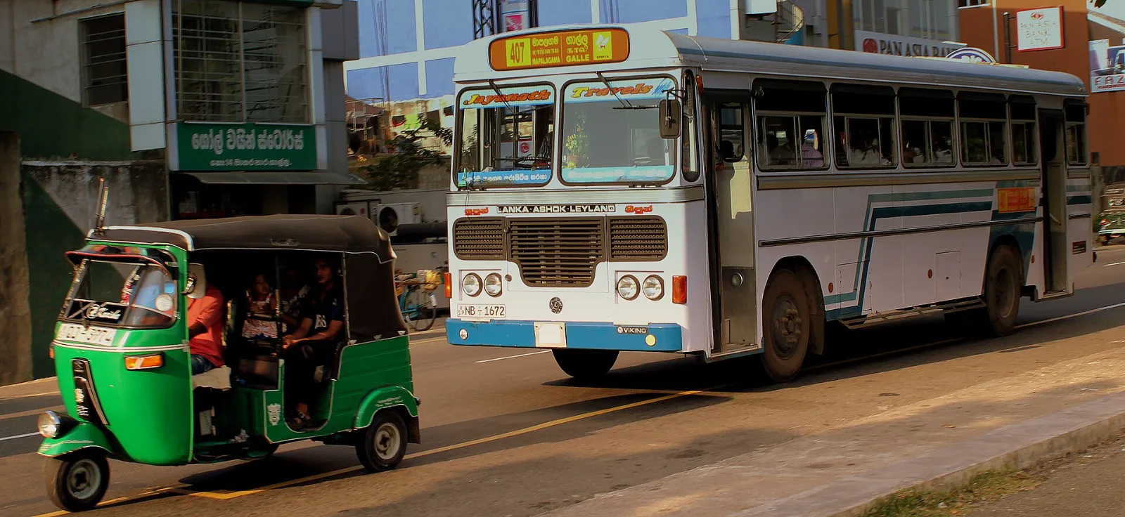 A Sri Lankan service bus and a tuk-tuk sharing the road
