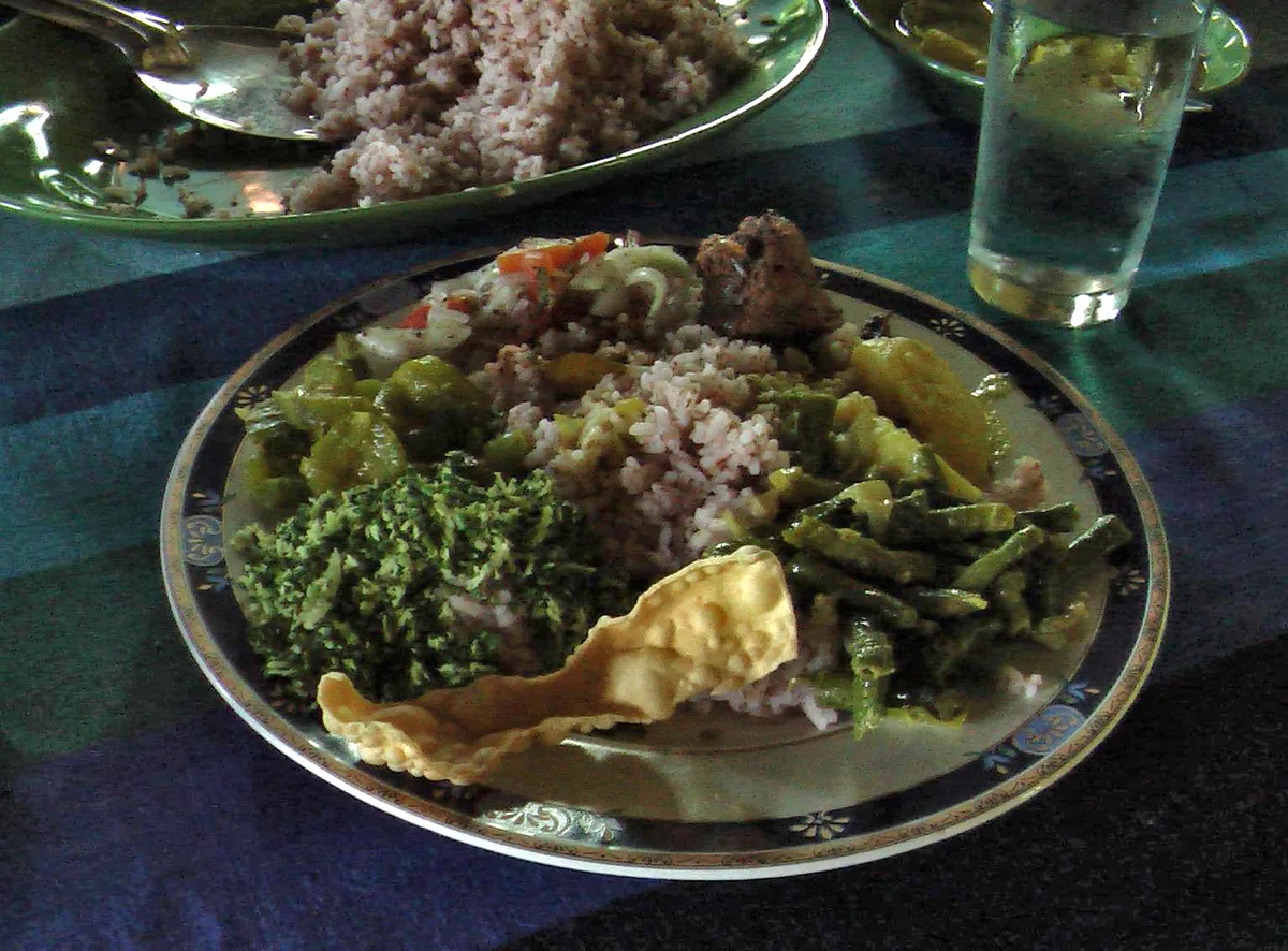 A plate of red rice with vegetable curries, gotukola sambol and a papadam
