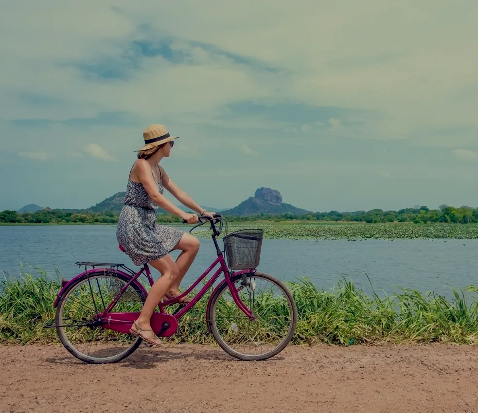 Cycling a dirt track beside a tank near Sigiriya, with Sigiriya Rock across the water
